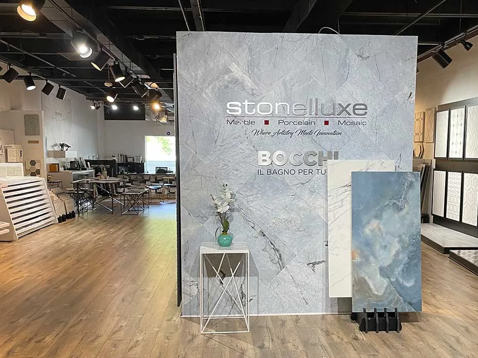 A large marble-printed wall in the Atlanta showroom carrying the Stonelluxe name and the line Where Artistry Meets Innovation, with slabs leaning against it.